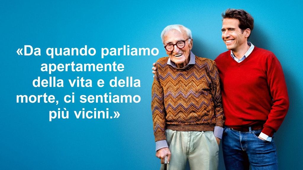 Il figlio mette un braccio sulle spalle del padre anziano. Sembrano soddisfatti. Immagine accompagnata dalla citazione: “Da quando parliamo apertamente della vita e della morte, ci sentiamo più vicini”.